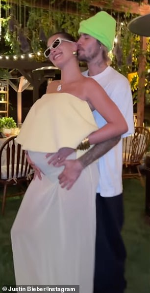 The Canadian pop star stands behind his wife, dressed in a relatively relaxed T-shirt and jeans, cradling her growing belly as she strikes a pose