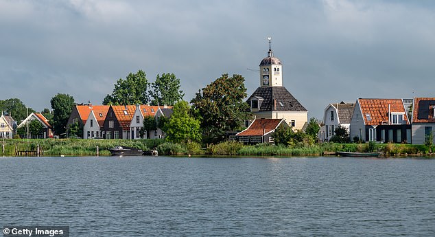 Pictured: Church and houses on the dike of the village of Durgerdam from the river Buiten IJ near Amsterdam, Netherlands