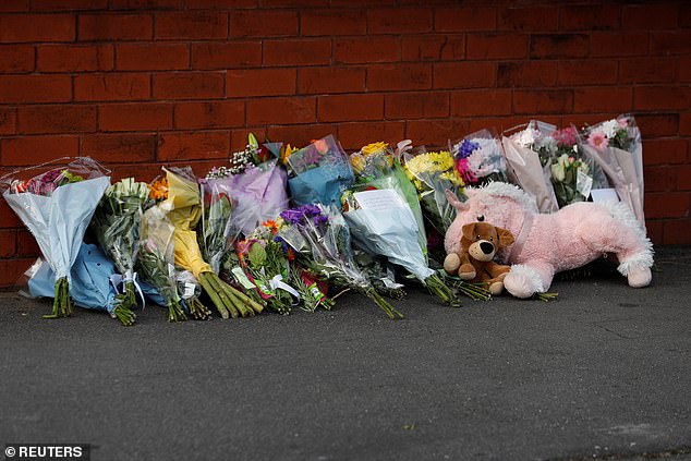 Flowers and a stuffed animal can be seen behind the police cordon