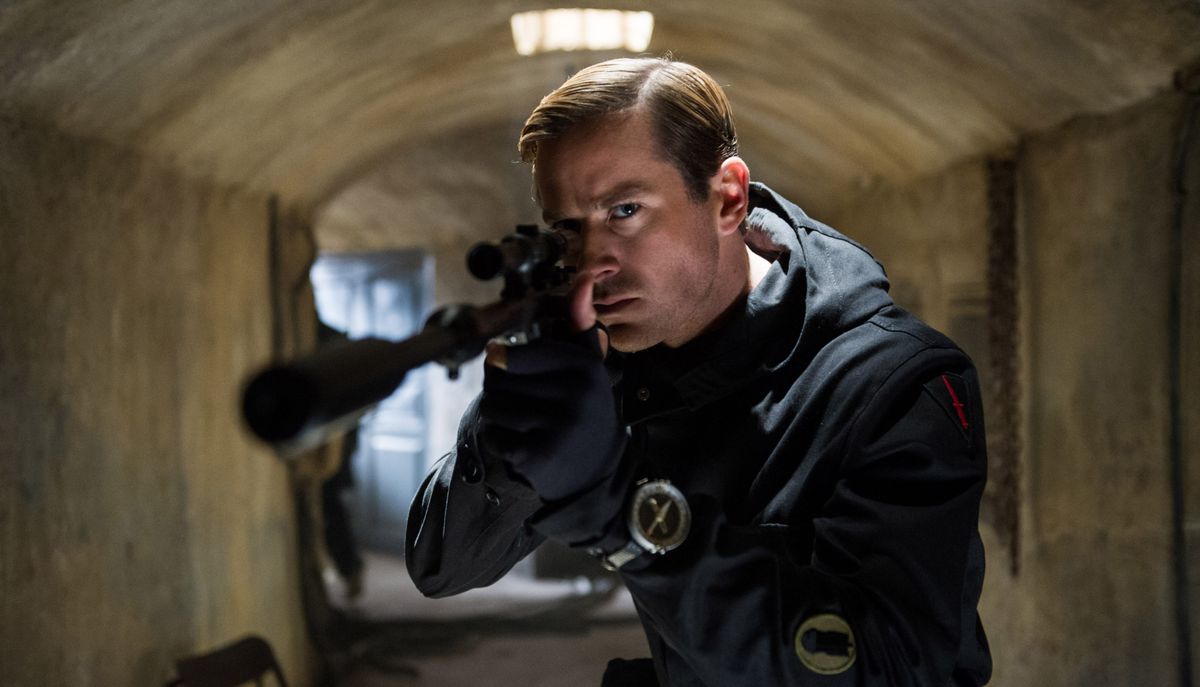 KGB agent Illya Kuryakin (Armie Hammer), dressed in black, stands in an underground concrete tunnel and points a sniper rifle at the camera in The Man From U.N.C.L.E.