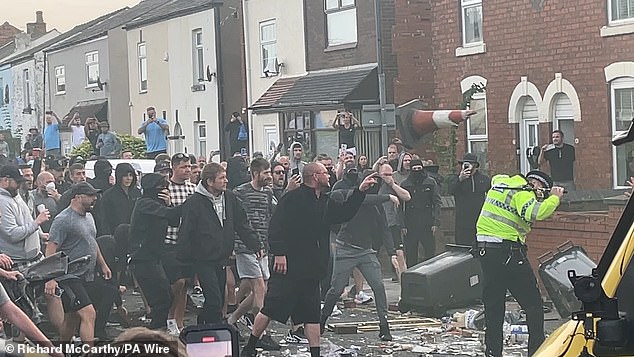 A masked man throws a traffic cone at a police officer near a mosque in Southport