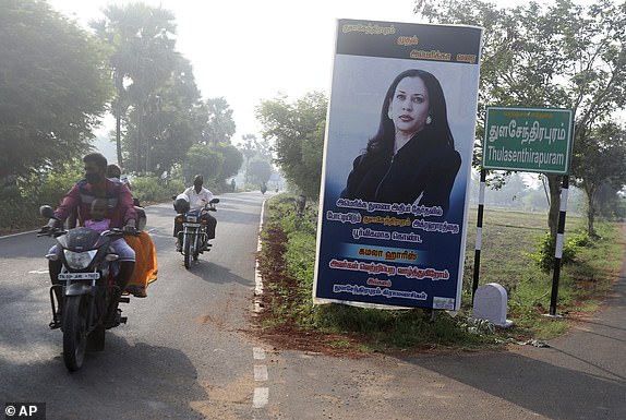 People drive past a billboard featuring U.S. Democratic vice presidential candidate Senator Kamala Harris at an intersection in Thulasendrapuram village, south of Chennai, Tamil Nadu state, India, Tuesday, Nov. 3, 2020. The lush green village is the birthplace of Harris' maternal grandfather who migrated from there decades ago. The billboard in Tamil reads: "From Thulasendrapuram to America we wish the American candidate for the vice-presidency, Kamala Harris, from the village of Thulasendrapuram, victory in the elections. From the villagers of Thulasendrapuram " (AP photo/Aijaz Rahi)