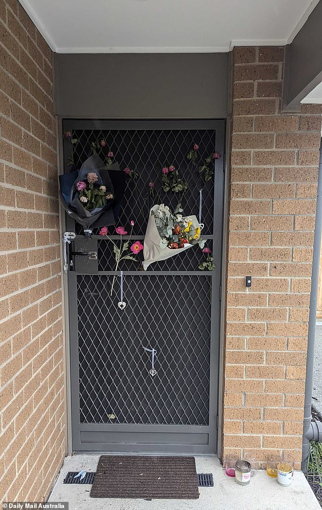 Tributes remain on the front door of the unit where four people died