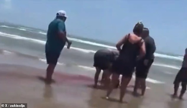 Blood can be seen from her wound as the water washing up on the beach turns dark red as rescuers wrap a tourniquet around her leg