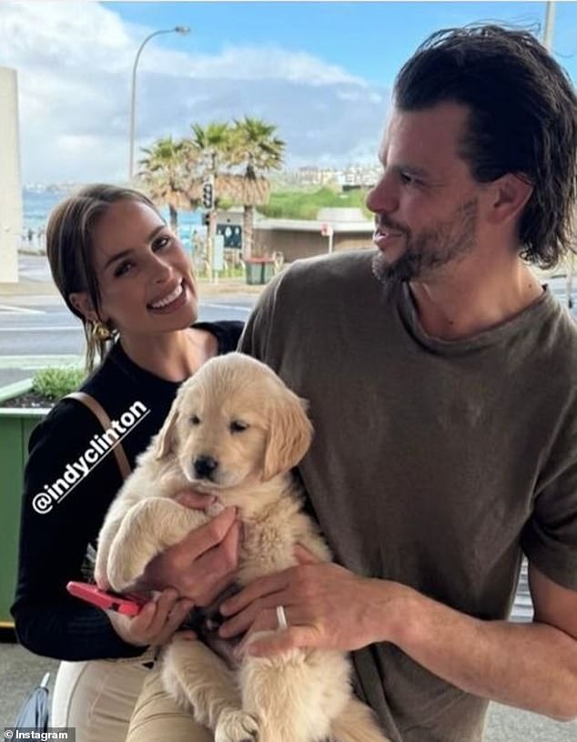 Indy Clinton has sparked a debate after admitting she plans to rehome her kelpie Billy after he bit one of her children. Pictured with new puppy and husband Ben Azar