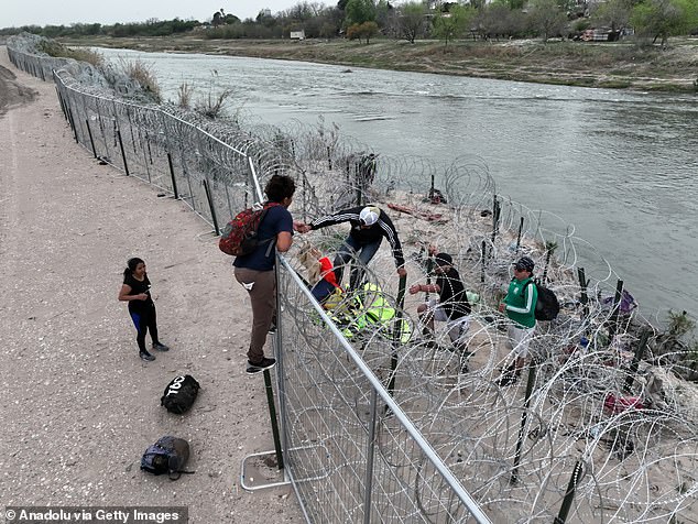 A group of illegal immigrants climb over a fence near Eagle Pass, Texas