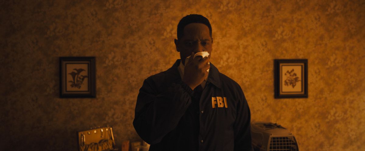 Blair Underwood as Agent Carter in Longlegs holds a cloth over his nose and watches an off-camera crime scene