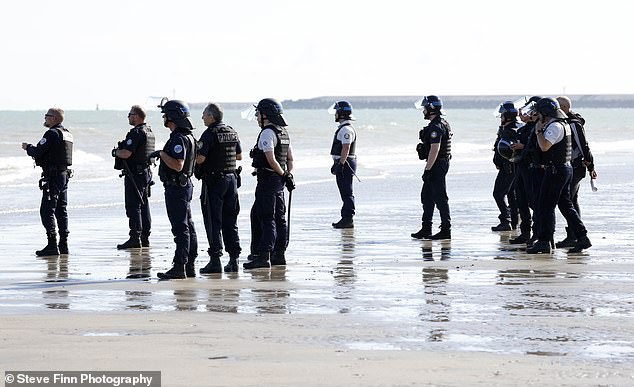 French police in riot gear watch as migrants enter the Channel in their overcrowded inflatable boat on July 11, 2024