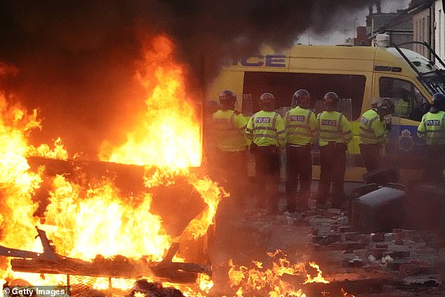 Riot police hold back protesters near burning police vehicle after disorder breaks out in Southport