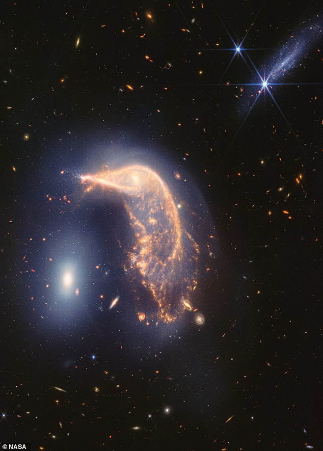 The orange spiral galaxy in the center has been distorted into the shape of a penguin by its interaction with the white elliptical galaxy on the left, which resembles an egg.