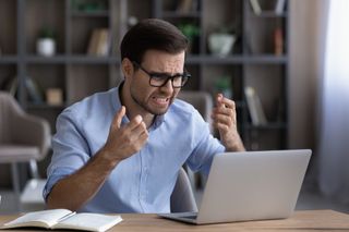 Unhappy male employee of millennial generation working online on laptop home office frustrated by gadget error or mistake. Angry young white man stressed by computer operational problem or malfunction.