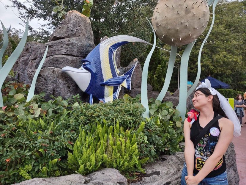 A sculpture of Gil from Finding Nemo. A woman in Bride Mickey Ears looks at it lovingly.