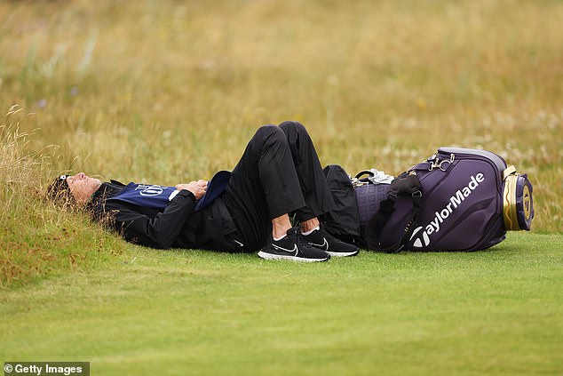 Ted Scott, Scottie Scheffler's caddie, lay down while waiting on the fifth green during Day 2