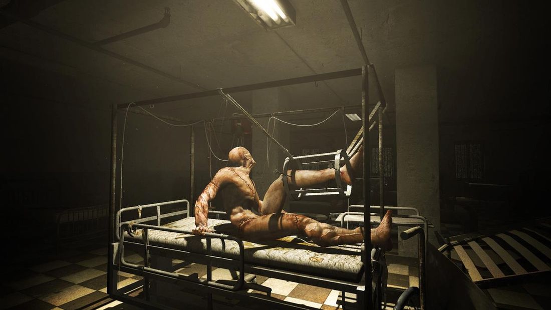 A screenshot from the horror game Outlast showing a naked person strapped to a stretcher, his body covered in scars