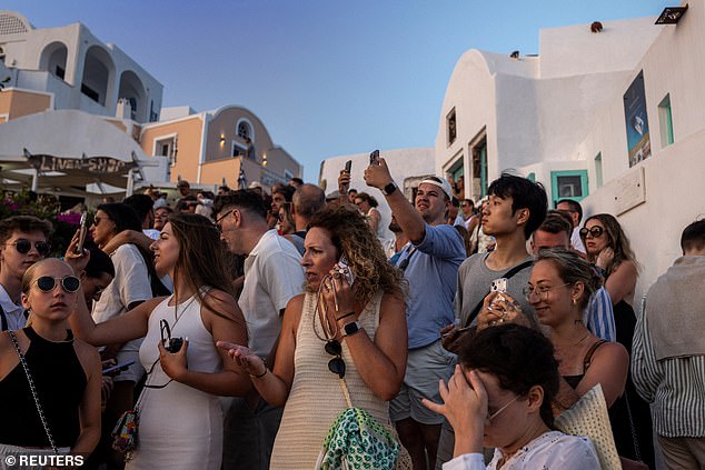 Hundreds of tourists sit on the steep hills of Santorini to watch and photograph the famous sunset on July 25, 2024