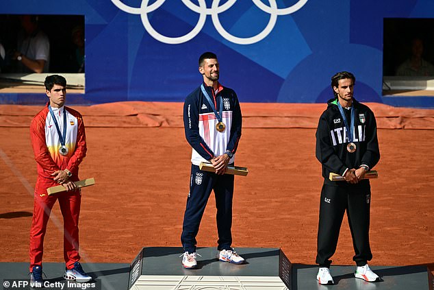 A grinning Djokovic stands on top of an Olympic podium, flanked by runners-up Alcarez (left) and Lorenzo Musetti (right) - who won the bronze medal for Italy