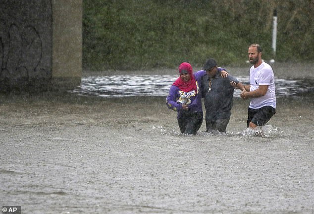 A man helps two people walk through floodwaters after their car became stuck on Vandeventer Avenue under I-64 (Hwy. 40) in St. Louis, Mo., on Thursday, July 28, 2022