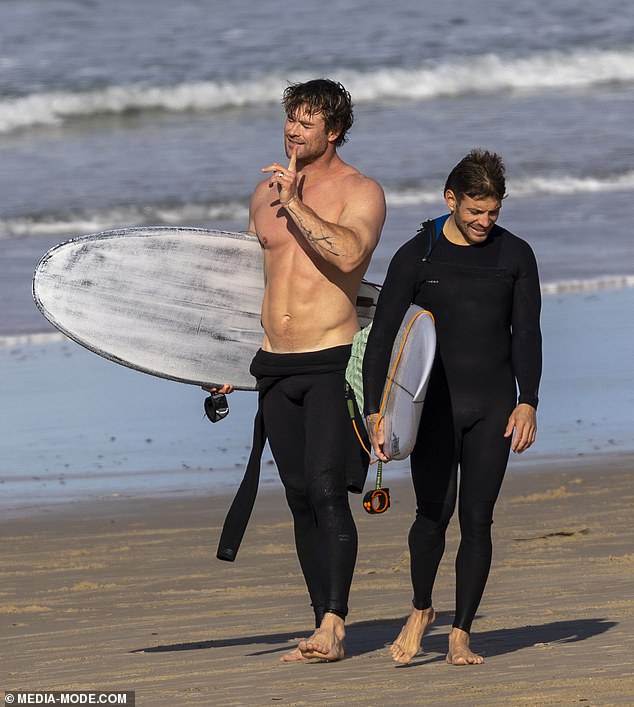 With a surfboard under his arm, the Hollywood star enjoyed his midwinter surfing with his good friend and personal trainer Luke Zocchi (right)