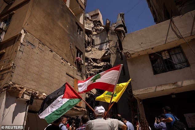 A man holds Palestinian, Lebanese and Hezbollah flags next to a damaged site where top Hezbollah commander Fuad Shukr was killed after an Israeli strike on July 30