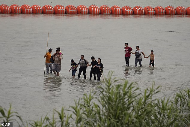 Migrants who crossed the Rio Grande from Mexico walk past large buoys placed as a border barrier