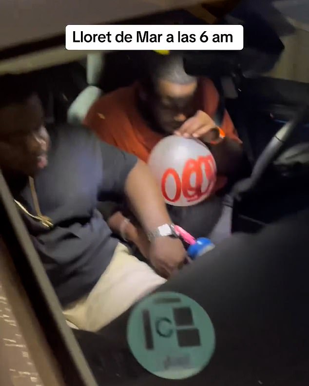 The person filming the car then walks over to the vehicle and sees that the driver (right) still has his seat belt on and is inhaling nitrous oxide.