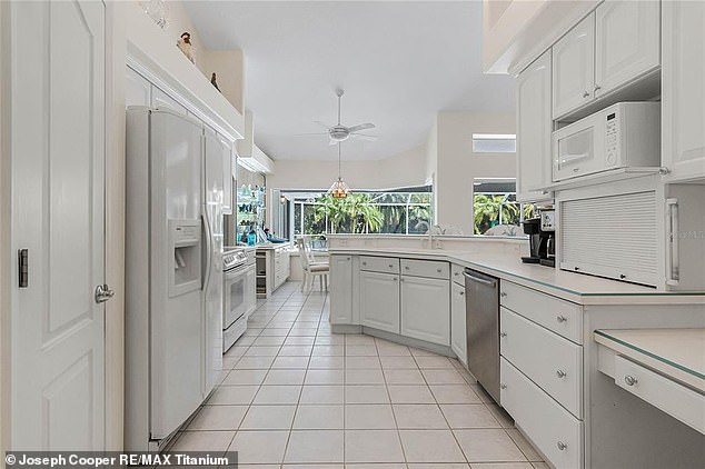 The main kitchen, which features white cabinetry and an island with seating, extends into a bright dining area overlooking the backyard and outdoor pool