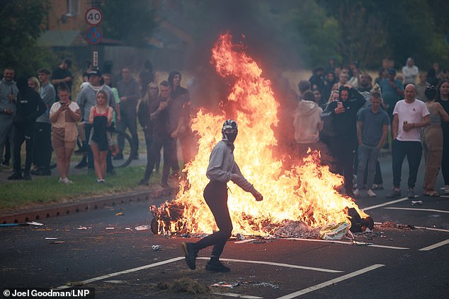 A masked rioter runs from a bonfire in the middle of a road in Rotherham on Sunday