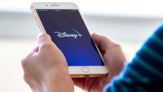 A person holding a smartphone with the Disney Plus app loaded on the screen