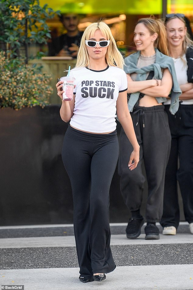 The former Fifth Harmony member, 27, wore a white ringer T-shirt with black lettering that read Pop Stars Suck while carrying a pink grocery store smoothie