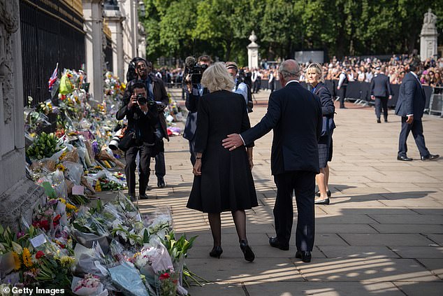 The new King Charles places an encouraging hand on Camilla's back as the couple view flowers and tributes laid outside Buckingham Palace following the death of Queen Elizabeth, September 2022