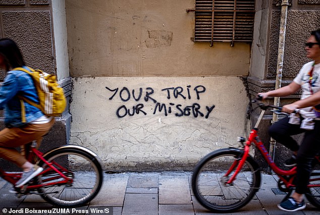 A group of tourists on a bike ride pass an anti-tourism graffiti that reads Your journey, our misery