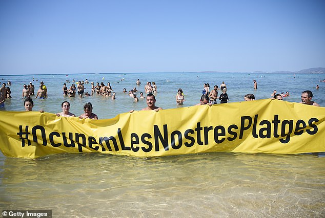 Members of the Mallorca Platja Tour association demonstrate against tourism with a banner reading 'Let's occupy our beaches!' on the beach of Palma de Mallorca on August 11