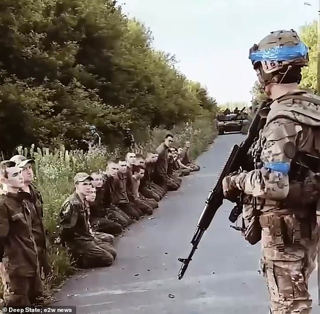 Ukrainian soldier stands guard as he monitors a line of Russian prisoners of war in Kursk