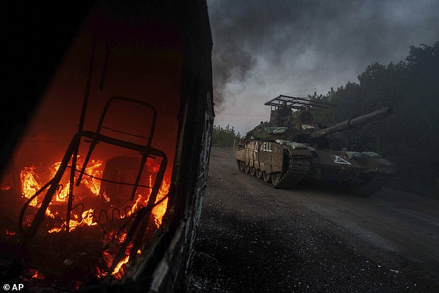 A Ukrainian tank passes a burning car near the Russian-Ukrainian border, Sumy region, Ukraine, Wednesday, August 14, 2024