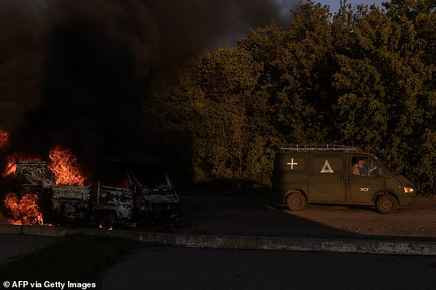 A Ukrainian military vehicle drives past a burning car on a road near the border with Russia, in the Sumy region of Ukraine, on August 14, 2024