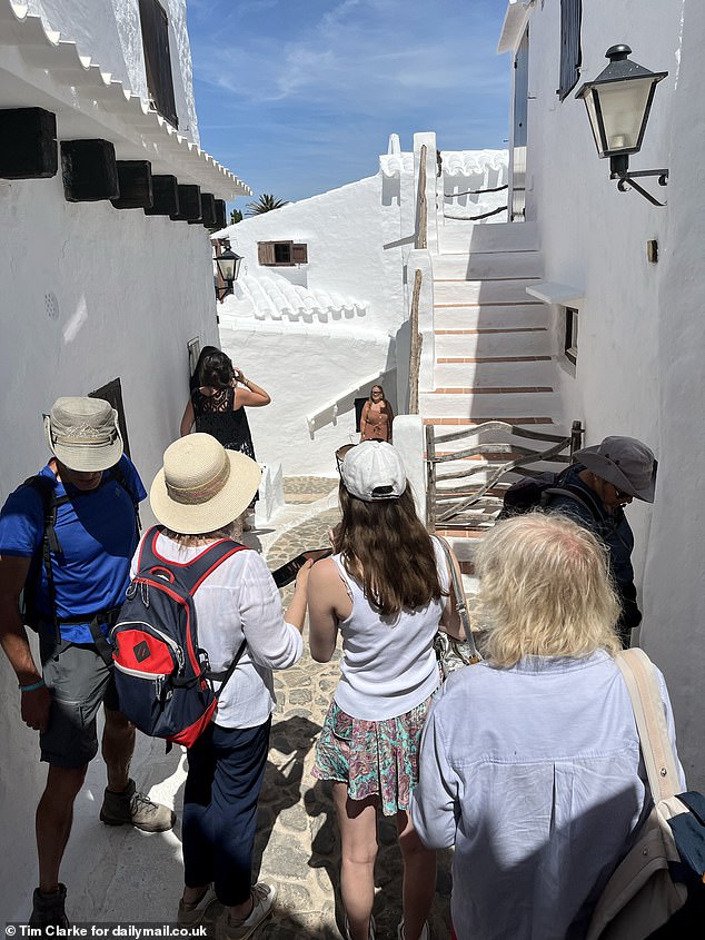 A horde of tourists are pictured in a small alley in the village taking pictures in front of the picturesque white stone houses