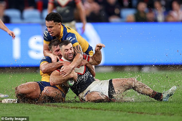 Roosters captain James Tedesco is tackled as mud and water splash from the surface