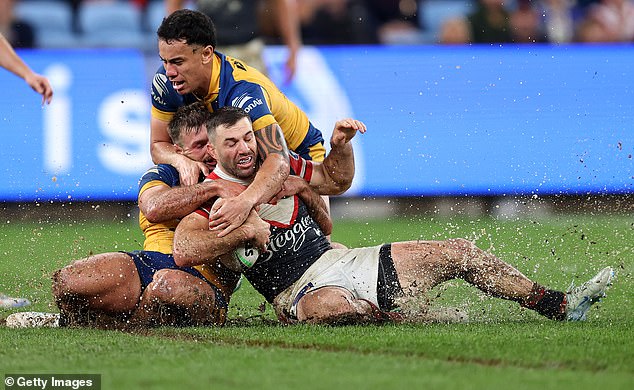 Roosters captain James Tedesco is tackled as mud and water splash from the surface