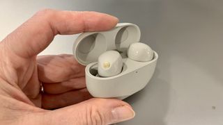 Someone holds the Sony WF-1000XM5 earbuds in their charging case against a gray background.