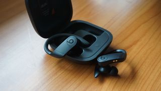 The Beats Powerbeats Pro earbuds next to their charging case on a wooden surface.