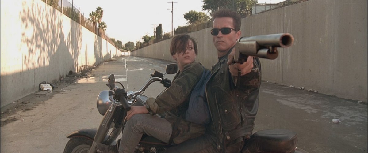 (L-R) Edward Furlong and Arnold Schwarzenegger as John Conner and a reprogrammed T-800 Terminator with a shotgun on a spinning motorcycle in a ravine in Terminator 2: Judgment Day. 