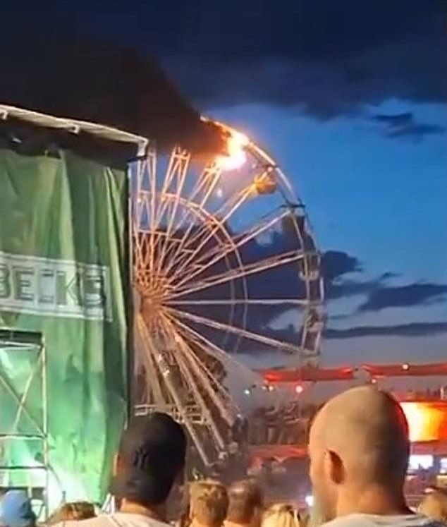 Black smoke rises from one of the upper carriages as festival-goers look on