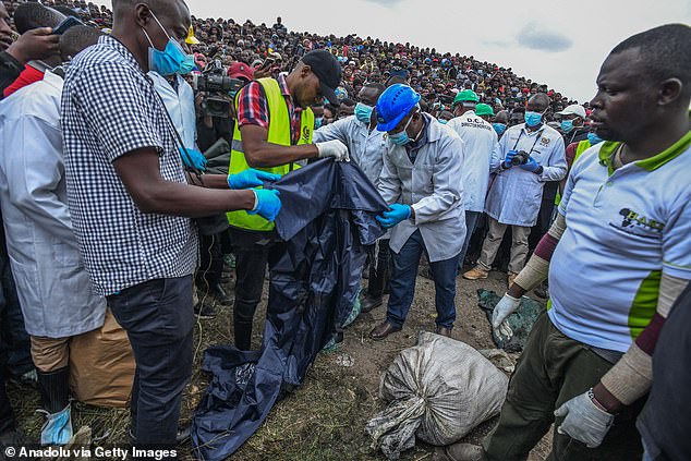 Officials inspect the bodies as they are watched by a crowd of local residents