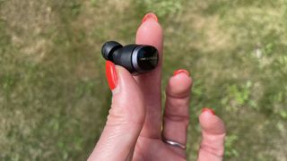 Bowers & Wilkins Pi8 earbuds held in a hand on a grassy background