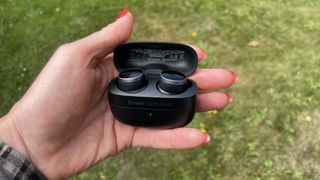 Bowers & Wilkins Pi8 earbuds held in a hand on a grassy background