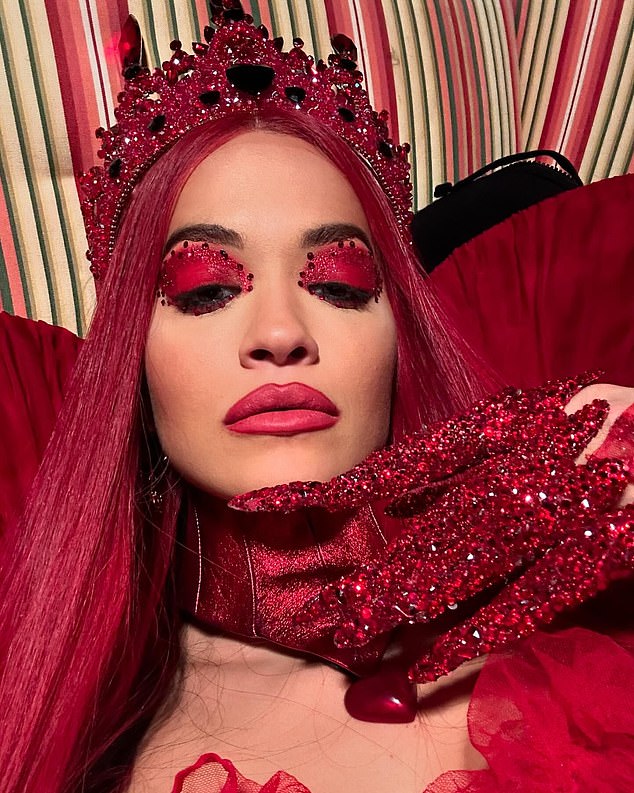 In one photo, Rita showed off her long crimson wig and matching jeweled crown, as well as her bright red eye shadow and matching lipstick, as she posed in a red pleated taffeta dress with a neck collar