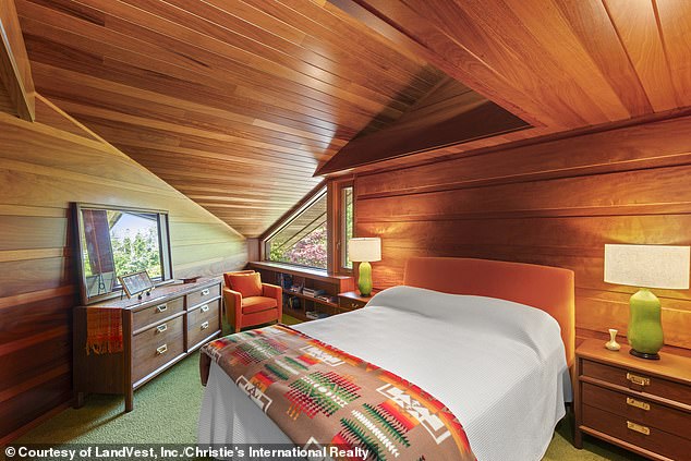 Another smaller bedroom, also clad in wood, features abstract sloped ceilings, windows and space for a queen-size bed