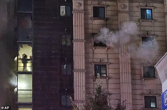 Firefighters work inside the building as smoke continues to billow from a nearby window