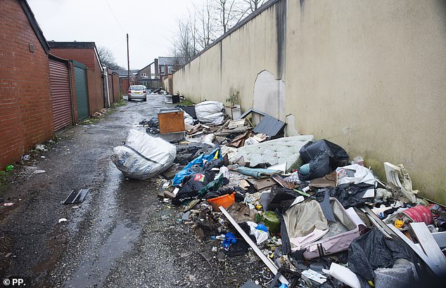 A filthy old mattress and an abandoned suitcase can be seen among huge piles of rubbish near the complex