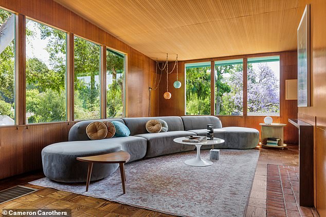 The living room features light wood paneling and ceilings and an abundance of large windows that let in plenty of sunlight